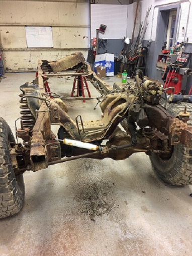 1993 Ford Bronco - The chassis and drivetrain of a vehicle are shown in a workshop setting, undergoing repairs or restoration.