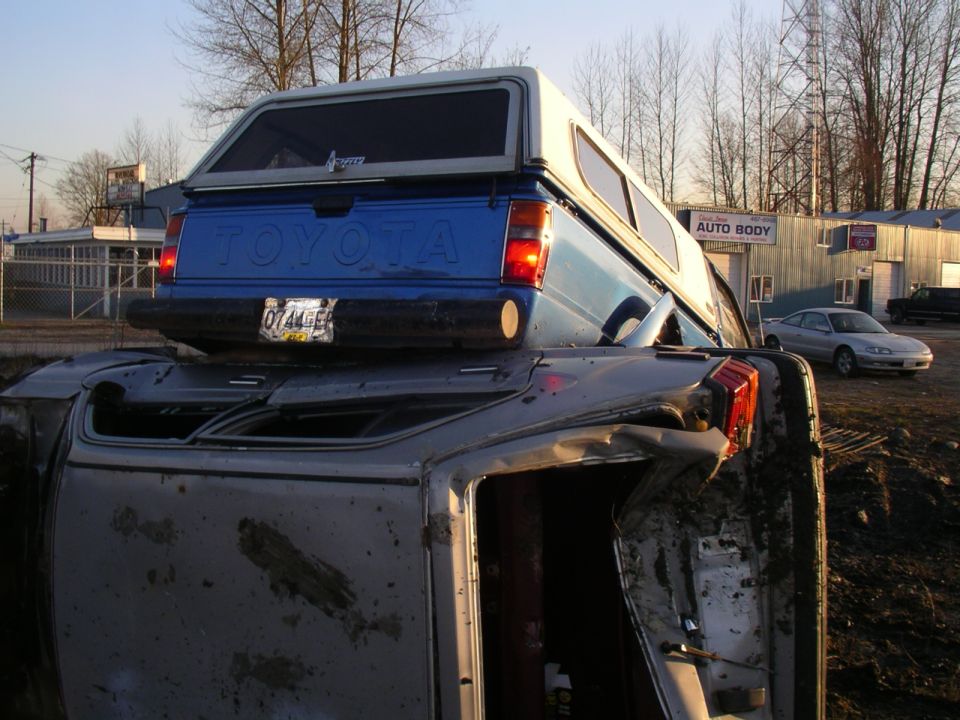 Blue Toyota pickup truck with camper shell on overturned vehicle
