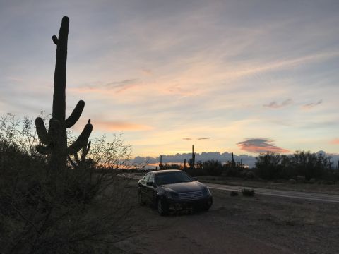 2007 Cadillac CTS - A sedan sits on a dirt road in the desert with saguaro cacti silhouetted against a colorful sunset sky.