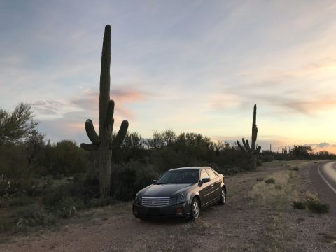 2007 Cadillac CTS - A dark gray 2007 Cadillac CTS sits parked on a dirt road beside a saguaro cactus as the sun sets in the desert.