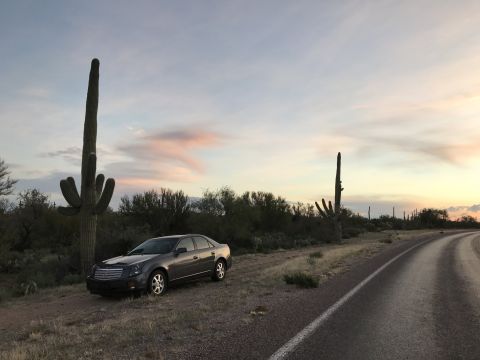 2007 Cadillac CTS - A 2007 Cadillac CTS sits parked on the side of a desert road at sunset, framed by saguaro cacti.