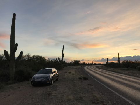 2007 Cadillac CTS - A 2007 Cadillac CTS sits beside a desert highway as the sun sets, casting pastel colors across the sky.