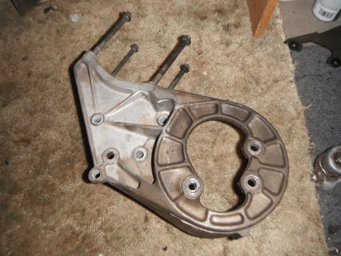 1990 Ford Bronco - A metal engine bracket with bolts is shown on a carpeted floor.