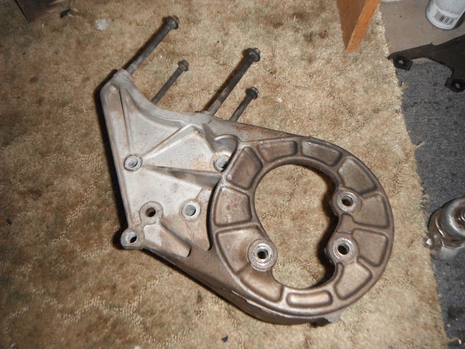 Engine bracket with three long bolts sticking out. It's sitting on a carpeted surface