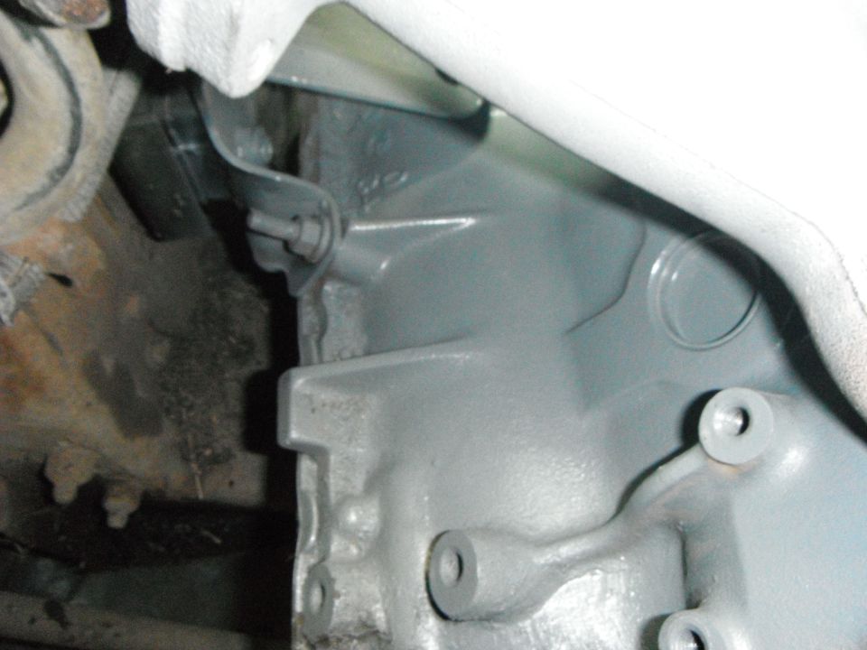 Gray painted engine part with bolts and brackets, rusty background, white pipe.