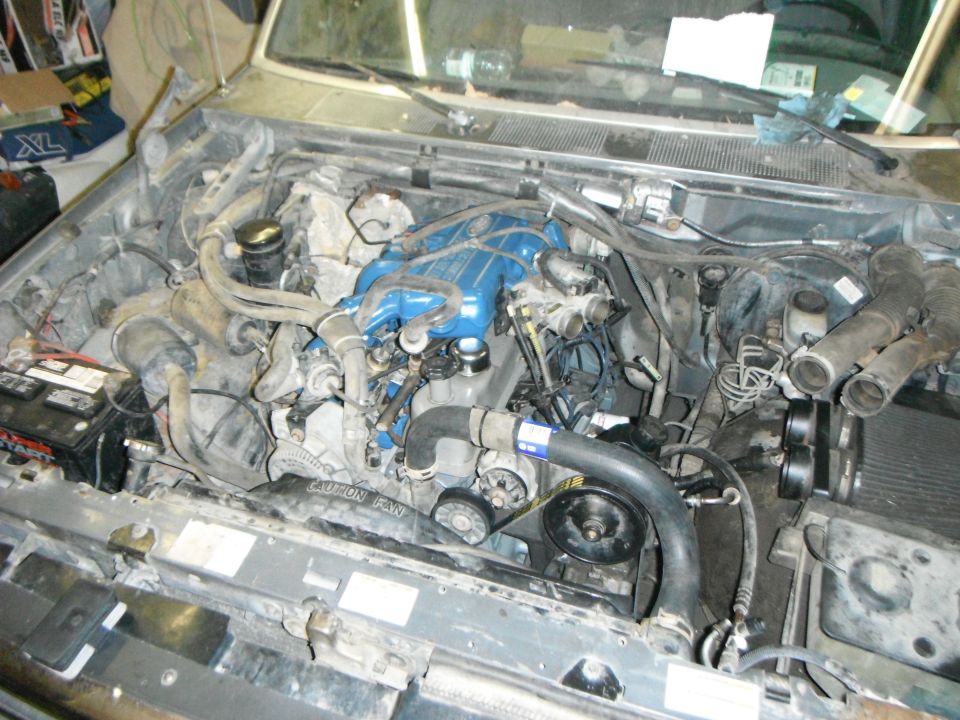 Engine bay of a Ford F-150 with blue intake manifold, battery, and hoses.