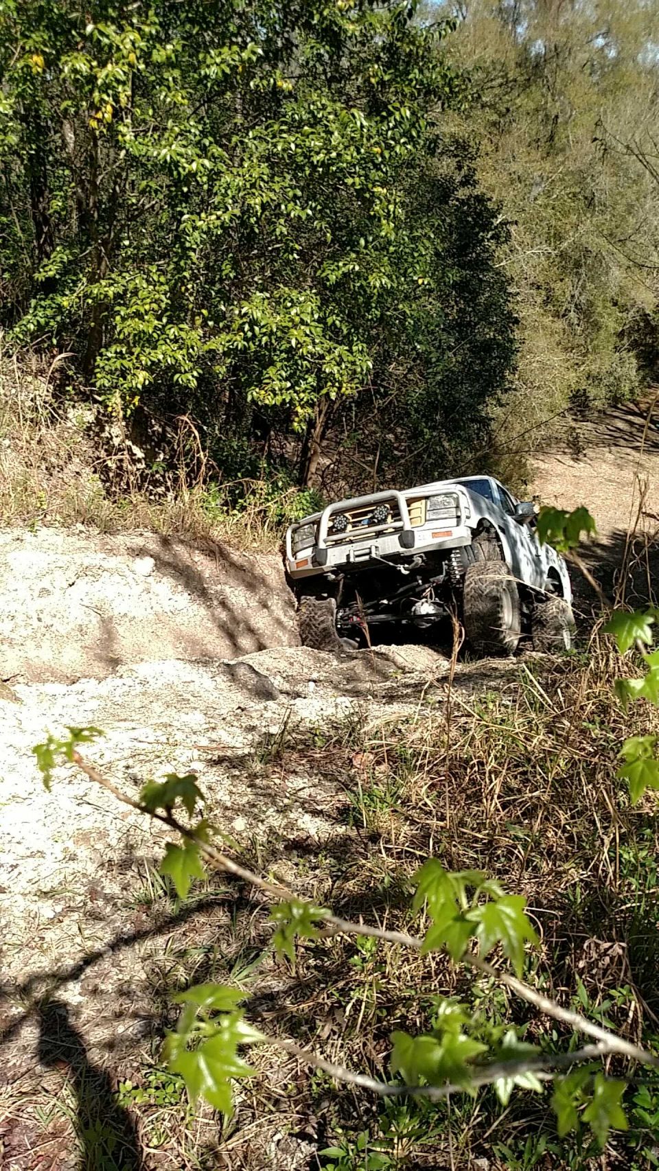 White 1990s Ford Bronco off-roading on a sandy hill.