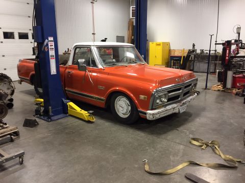 1984 Ford Bronco - A lowered, orange and white GMC pickup truck is parked on a hydraulic lift in a garage. The truck has chrome trim and a white roof.