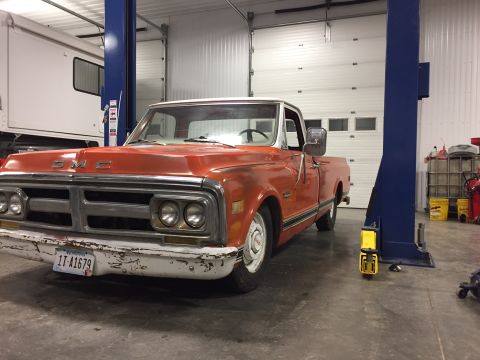 1984 Ford Bronco - A vintage orange GMC pickup truck is parked in a garage, possibly on a lift. The truck has a white roof and bumper, and a Montana license p…