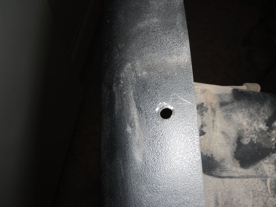 Black textured panel with a hole next to a dusty vehicle part.