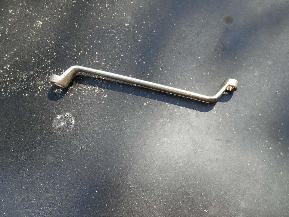 Silver bent wrench on a dark, textured surface with debris