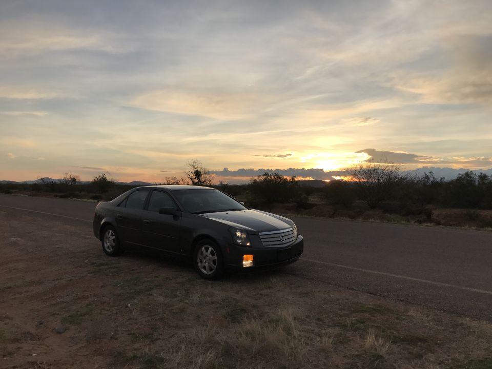 2007 Cadillac CTS sedan parked on a dirt roadside at sunset.