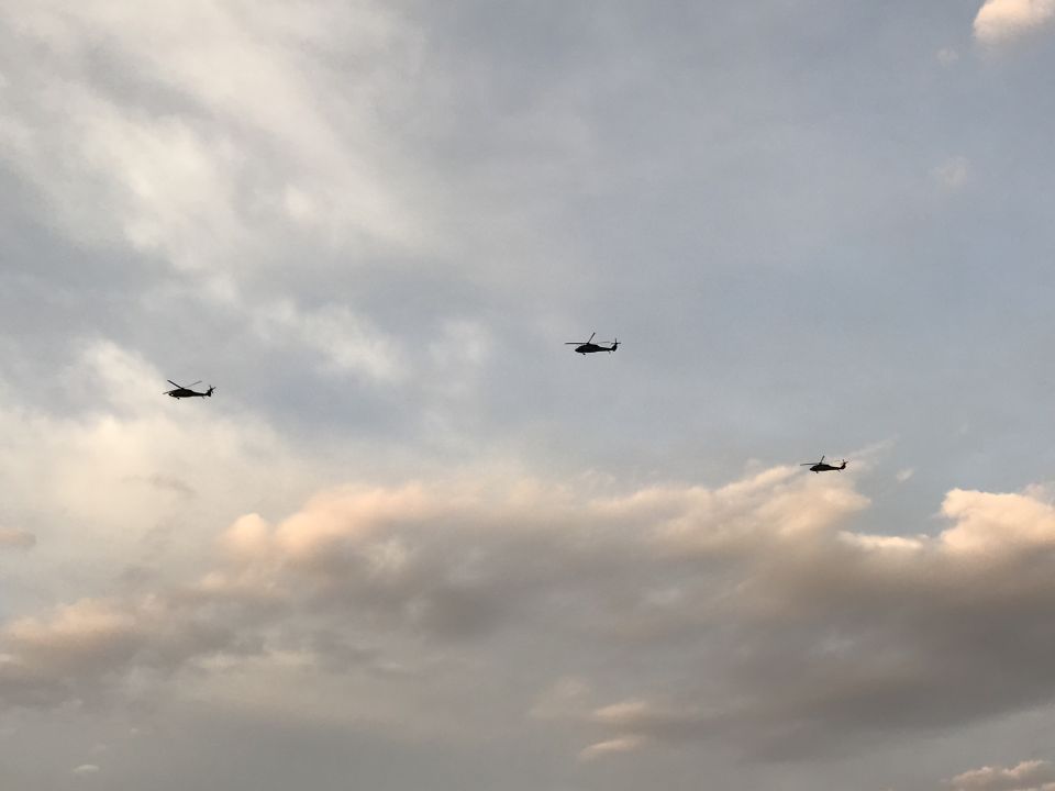 Three helicopters flying in formation against a cloudy sky.