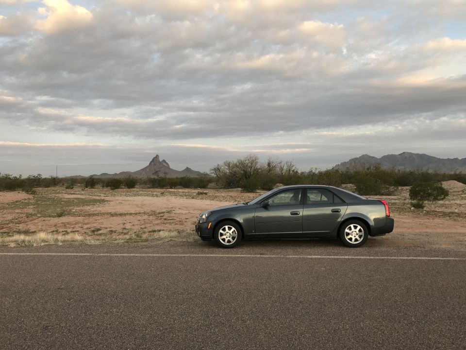 2007 Cadillac CTS sedan parked on a desert roadside with mountains in the background.