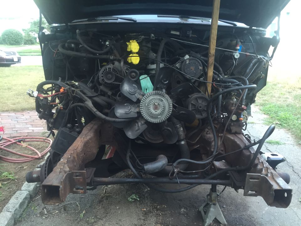 1995 Ford Bronco engine bay with hood open, engine disassembled, supported by jack stands.