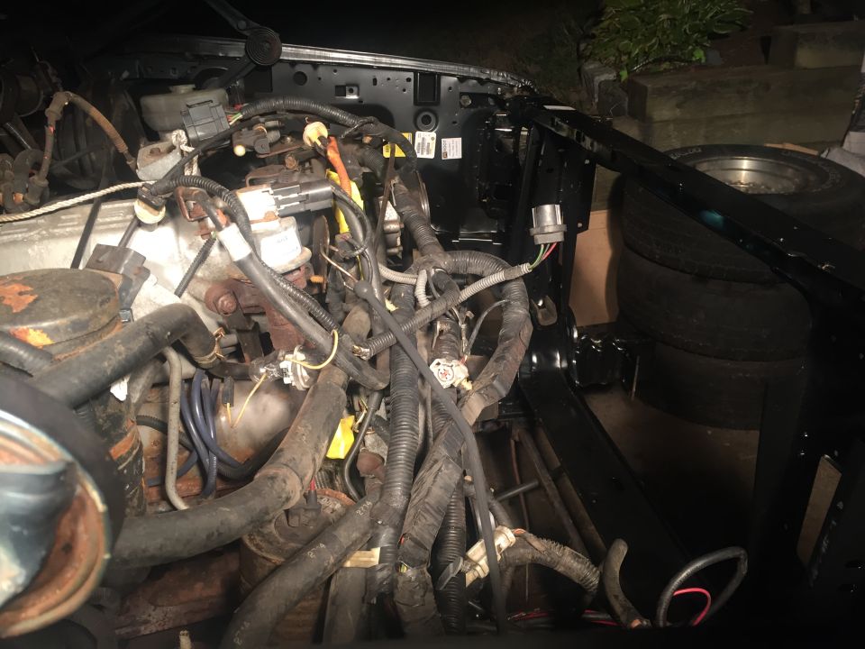 Vehicle engine bay with hoses and wires, tires in background