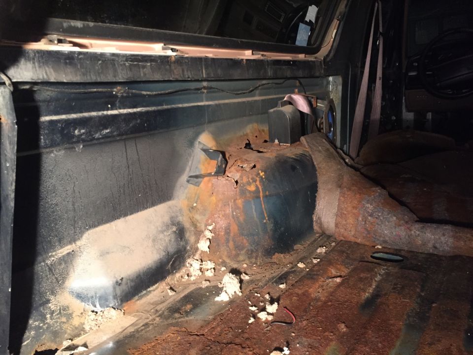 Interior of a rusted 1995 Ford Bronco showing floor pan and transmission tunnel.