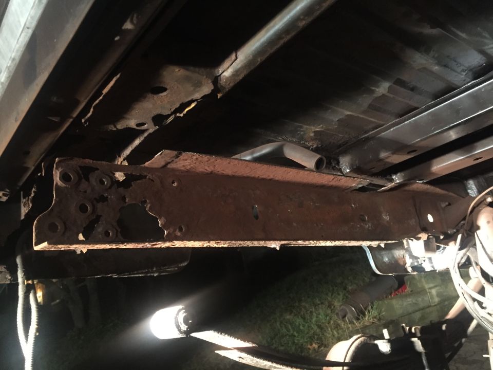 Heavily rusted and damaged vehicle frame rail with exhaust pipe.