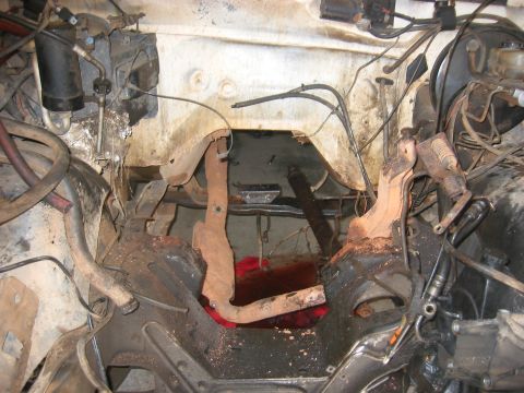 1989 Ford Bronco - Underside view of a vehicle's engine bay, revealing the pedals and transmission tunnel, with a noticeable spill of red fluid.