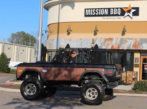 1972 Ford Bronco - A lifted, two-tone brown and black 1972 Ford Bronco is parked in front of a Mission BBQ restaurant. The Bronco has large off-road tires and…