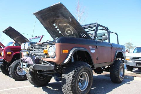 1972 Ford Bronco - A brown 1972 Ford Bronco with its hood open is parked next to a red vehicle. The Bronco has a custom front bumper and large off-road tires.