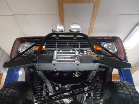 1972 Ford Bronco - Low-angle view of the front of a vintage Ford Bronco, lifted and modified with a heavy-duty winch bumper, brush guard, and auxiliary lights…