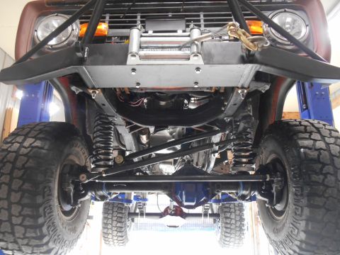 1972 Ford Bronco - Underside view of a lifted 1972 Ford Bronco showing the front suspension, differential, and large off-road tires. The vehicle has a custom…