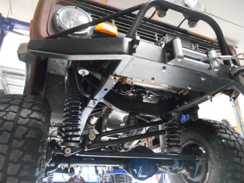1972 Ford Bronco - Underside view of a vintage Ford Bronco with significant suspension modifications including large coilover shocks and a custom front bumper…