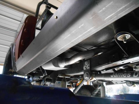 1972 Ford Bronco - The underside of a vehicle, likely a 1972 Ford Bronco, shows a custom exhaust system with a muffler and a long metal component with the tex…