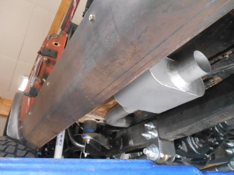 1972 Ford Bronco - Underside view of a vehicle, showing a custom exhaust system with a muffler mounted to the frame. A large metal plate is bolted along the s…