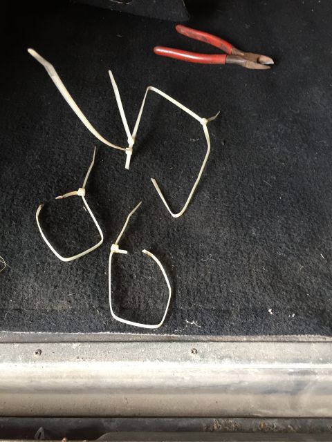 1979 Ford Bronco - A pair of red-handled wire cutters rests on a black carpeted surface next to several cut white zip ties. The scene appears to be inside a v…
