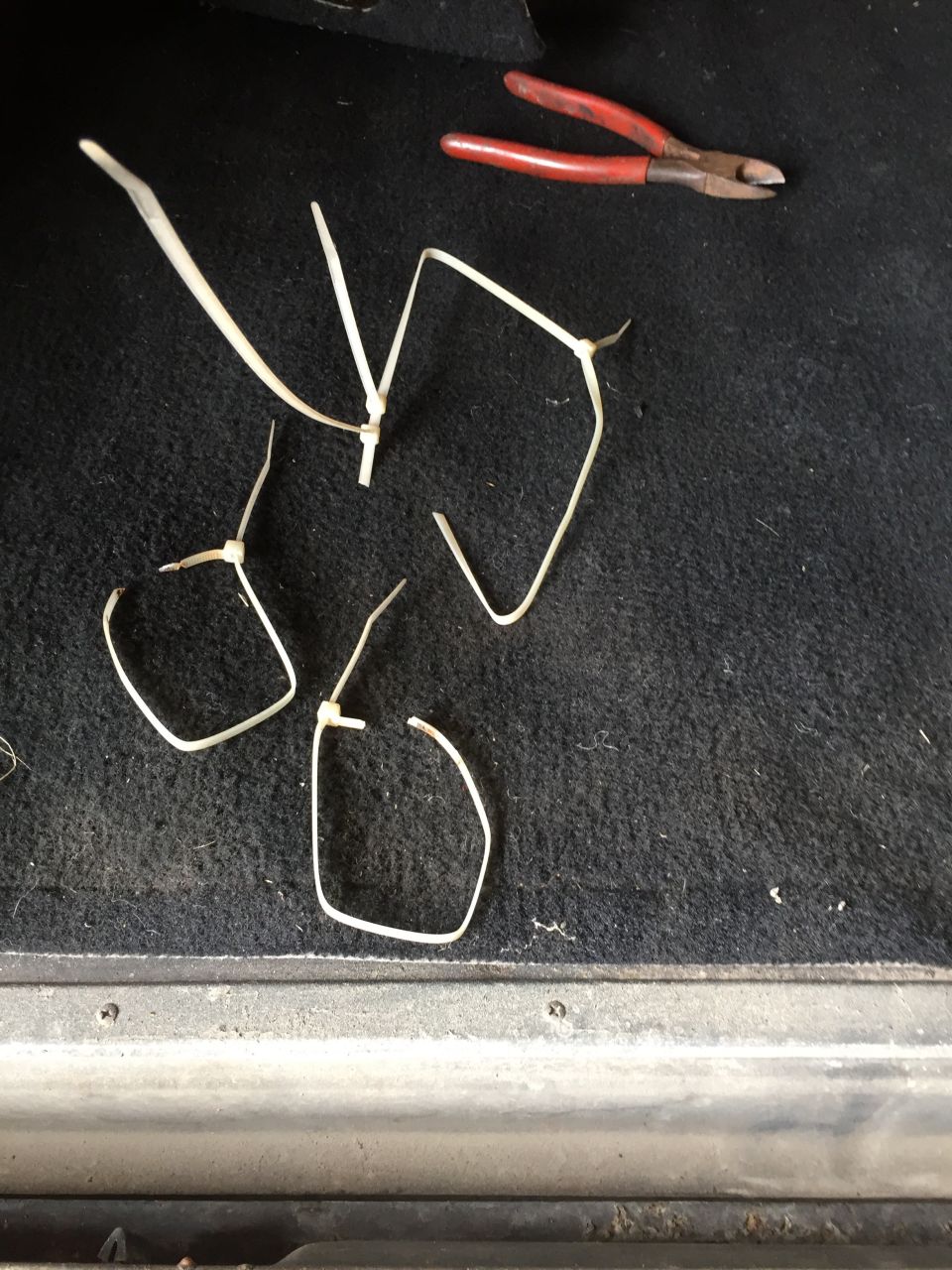 Red-handled wire cutters and cut white zip ties on black carpet.