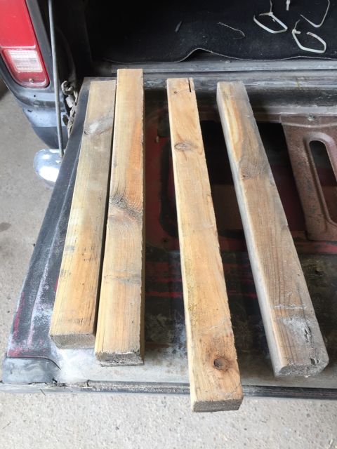 1979 Ford Bronco - Four wooden planks are laid across the bed of a red pickup truck. The truck's tailgate and rear bumper are visible.