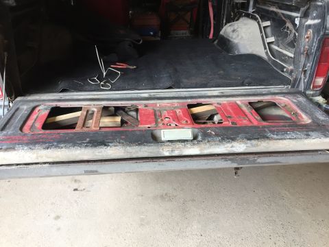 1979 Ford Bronco - The open tailgate of a classic pickup truck bed shows a black carpet liner and some tools. The red tailgate itself has two large rectangula…