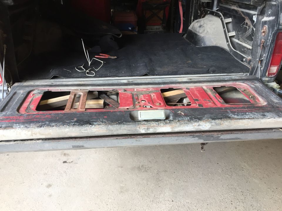 Open tailgate of a red and black pickup truck showing carpet, tools, and cutouts in the tailgate.