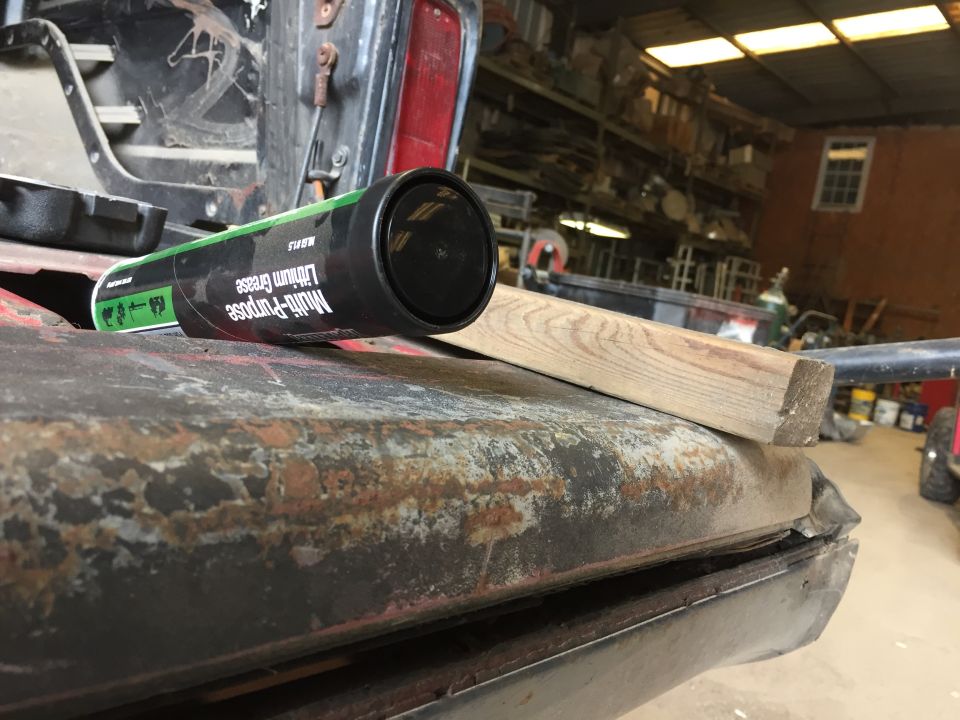 Grease tube on rusted vehicle panel with wooden block in workshop