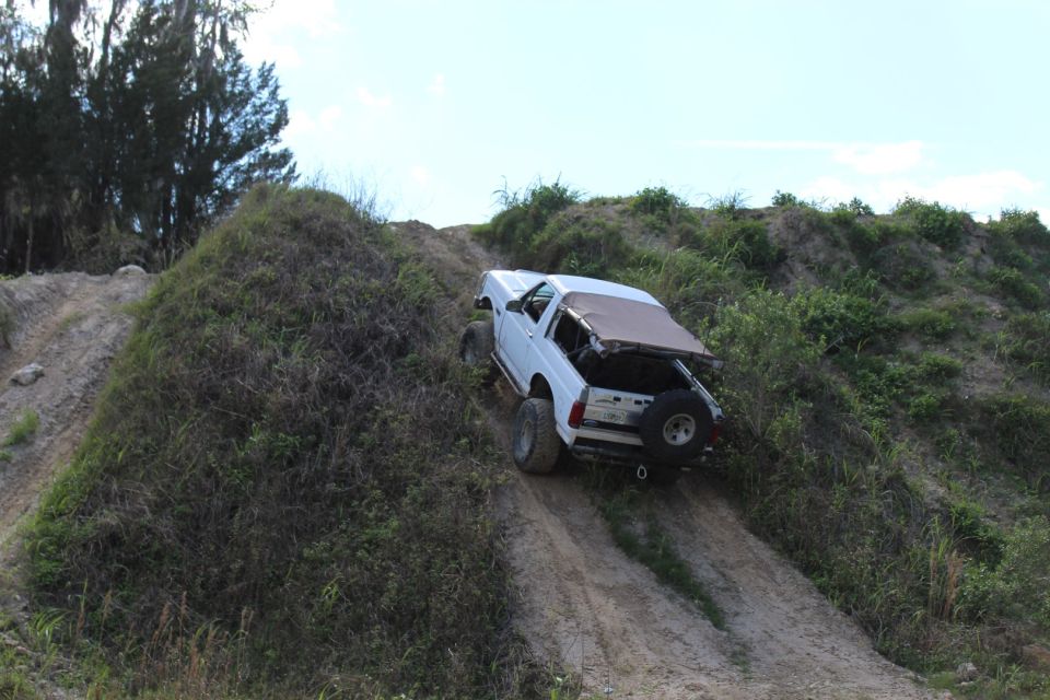 White Ford Bronco driving up a steep, grassy dirt hill, rear-three-quarter view.