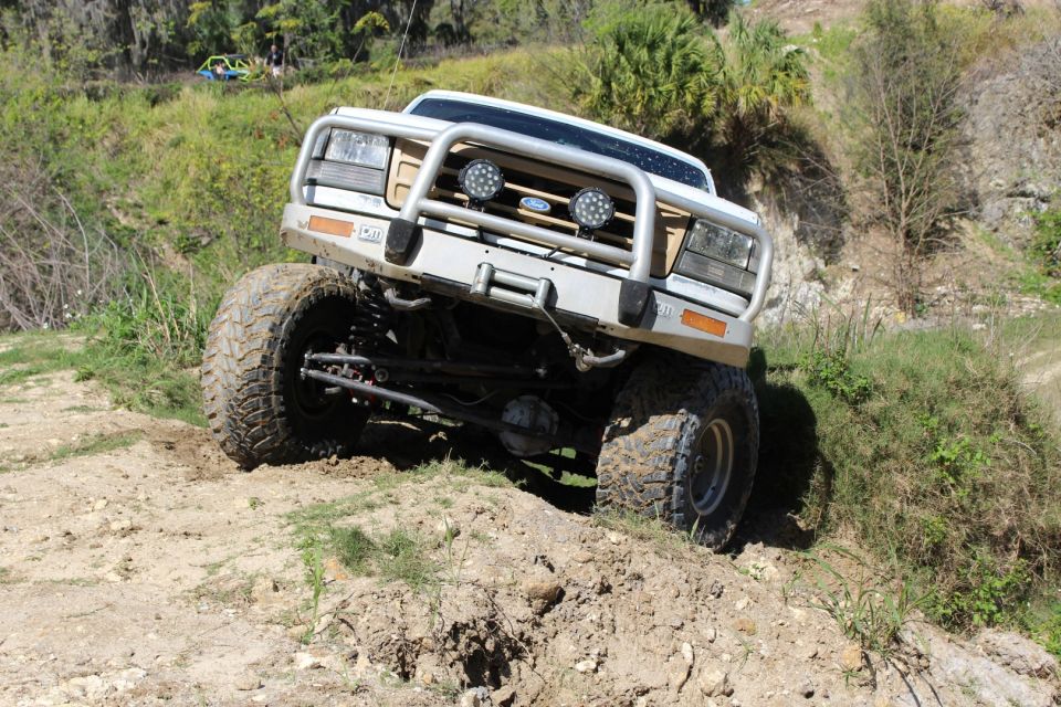 1992 Ford Bronco climbing a dirt hill, front right wheel elevated, with a brush guard.