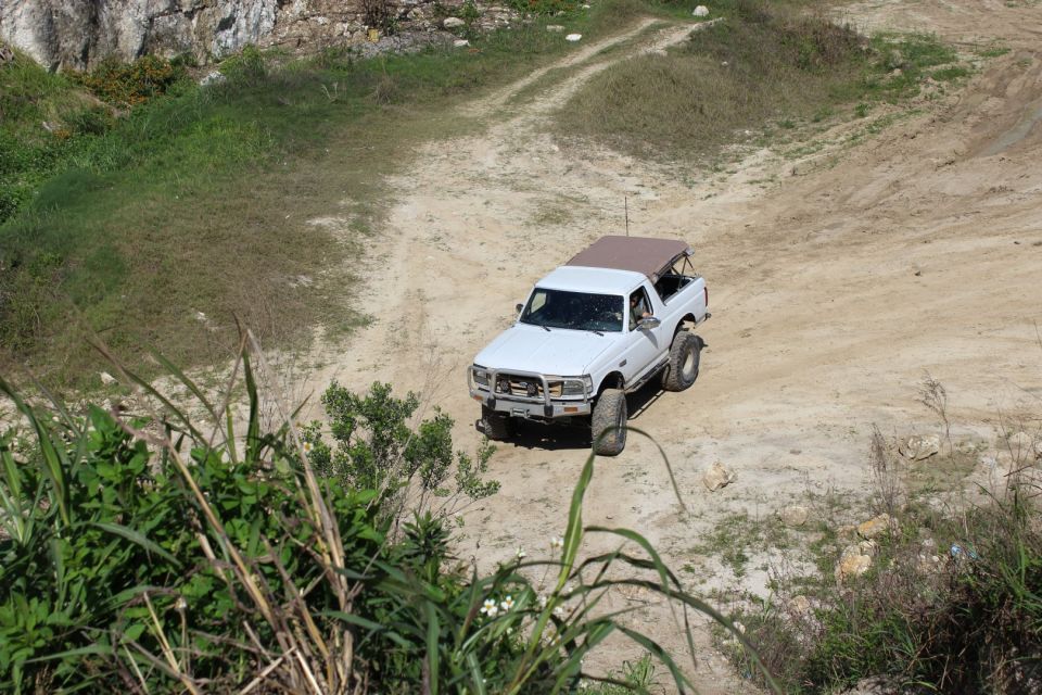 White Ford Bronco with brown soft top driving on a dirt path in a quarry.