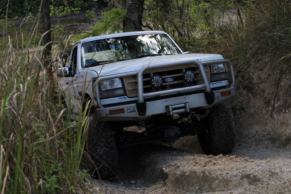 Silver 1992 Ford Bronco driving on a dirt path with brush guard and winch.