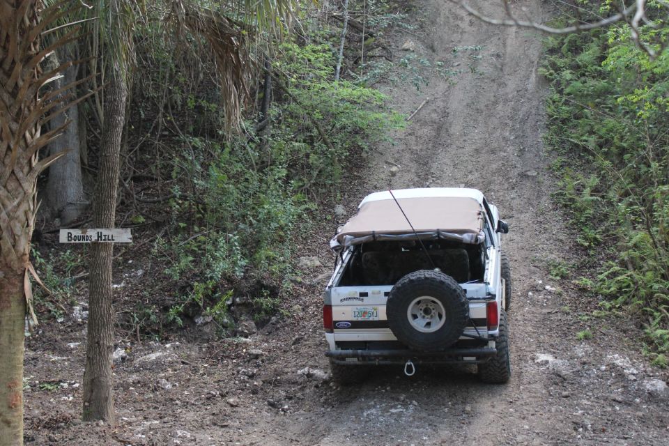 White Ford Bronco with rooftop tent driving up a steep dirt trail.