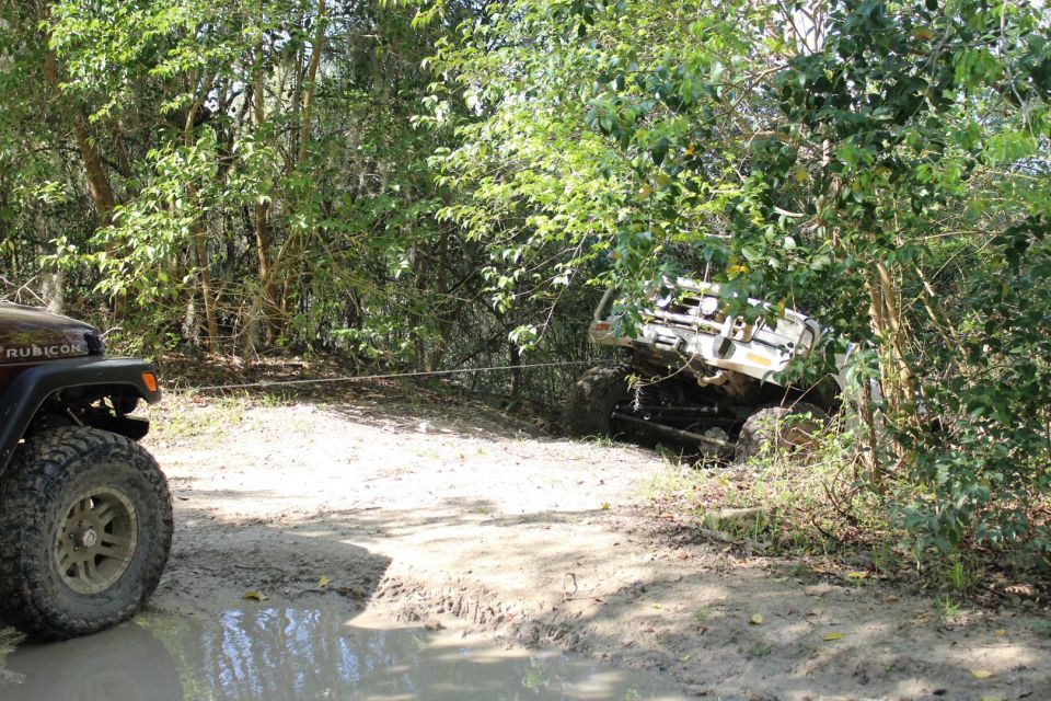 Two Jeeps in a muddy, wooded area, one being winched.