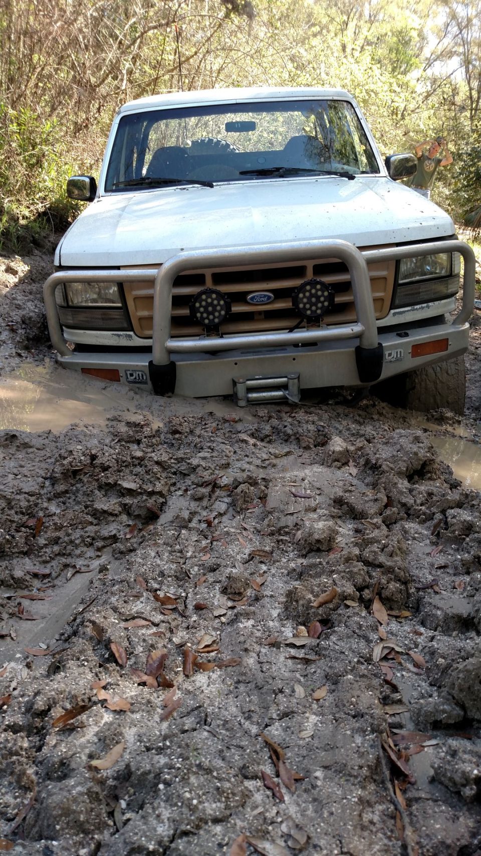 White Ford Bronco stuck in mud, front view.