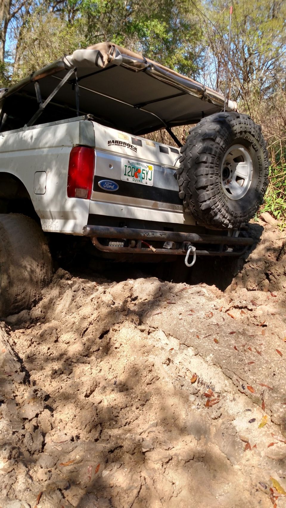 White Ford Bronco stuck in mud, rear view with spare tire and Florida license plate.