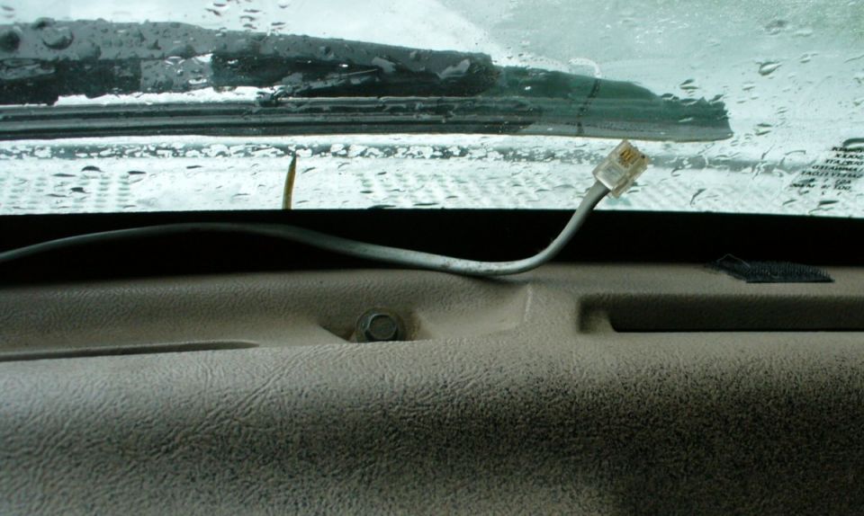 Tan dash top and rainy windshield with a gray cable and RJ11 connector routed along the base of the glass