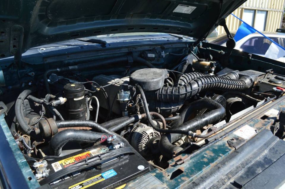 Engine bay of a dark green 1995 Ford Bronco, showing air intake, battery, alternator, hoses.