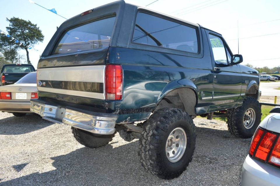 Lifted dark green 1995 Ford Bronco rear passenger side with large off-road tires and chrome bumper.