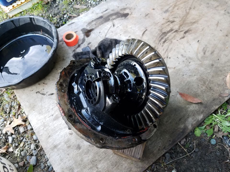 Disassembled differential assembly with gears, covered in black grease, outdoors next to an oil drain pan.
