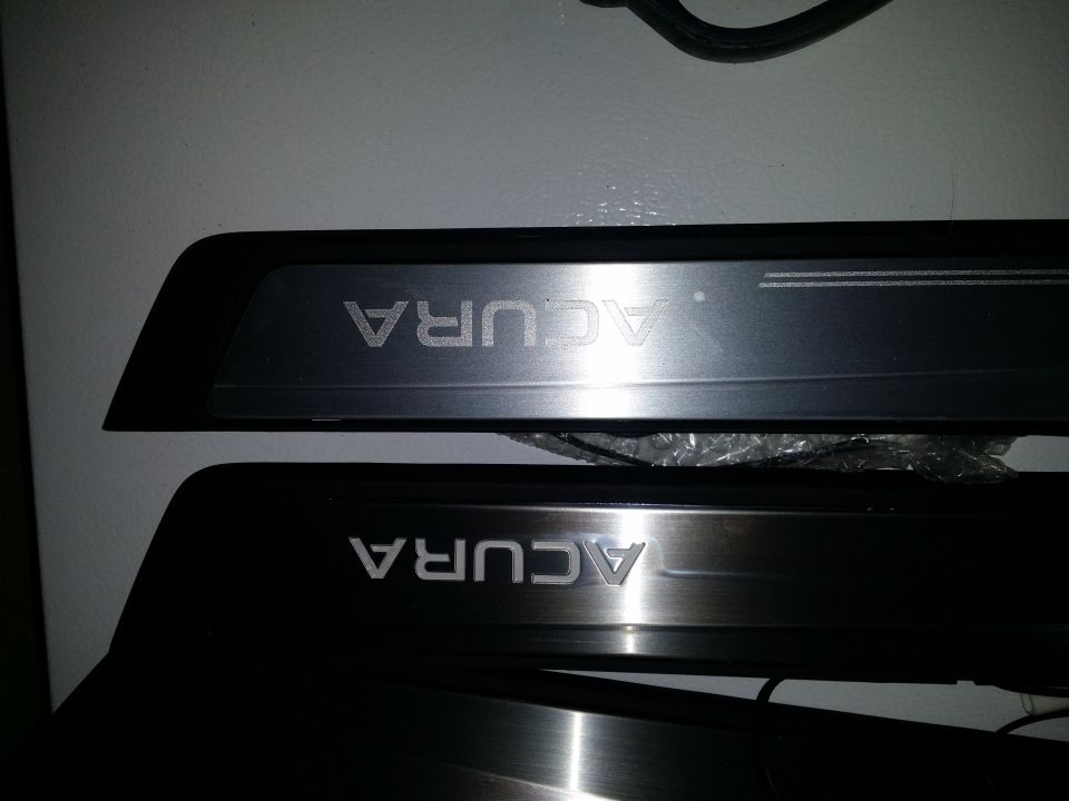 Two Acura door sill plates, one lighter and one darker brushed metal.