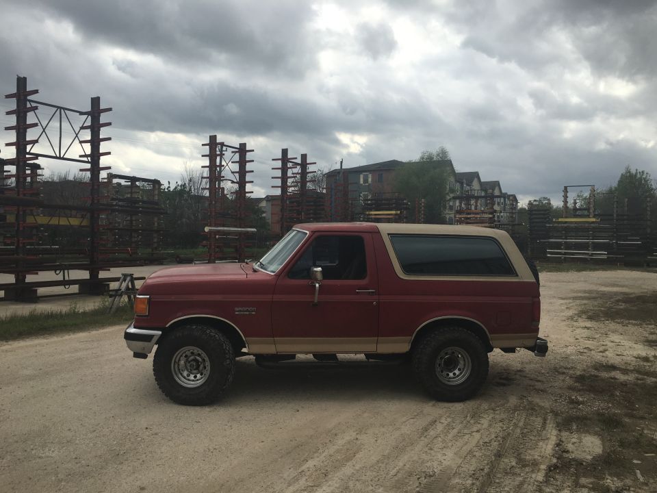 Red and tan 1990 Ford Bronco parked on a dirt lot.